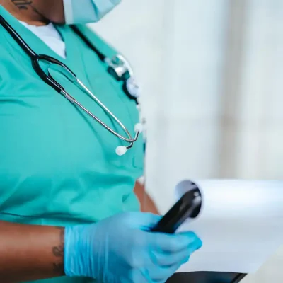 A Black healthcare professional is wearing blue scrubs and reading a medical chart.