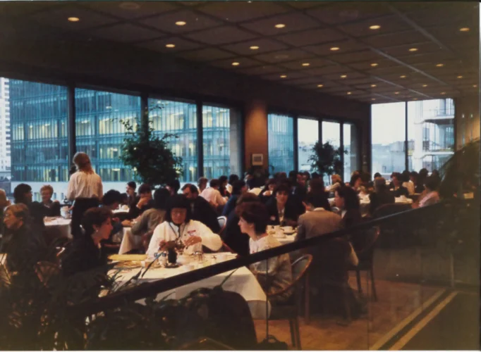 A room with tables covered with white tablecloths is filled with people gathering to celebrate the Equality Breakfast in 1998.