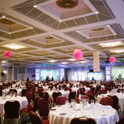 A huge banquet hall in the Fairmont Hotel Vancouver with white table cloths and pink balloons with an ornate ceiling.