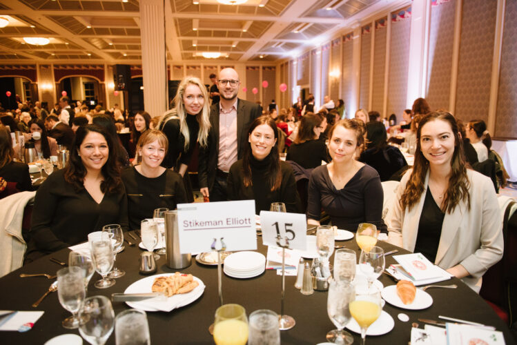 A group of Equality Breakfast attendees smile while sitting around a large table.