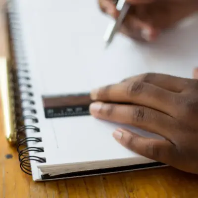 A close up shot of a Black person drawing in a notebook with a ruler.