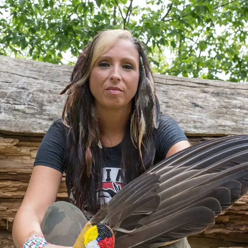 Indigenous lawyer and advocate Pam Palmater sits in front of a tree holding an eagle feather with medicine wheel beading.